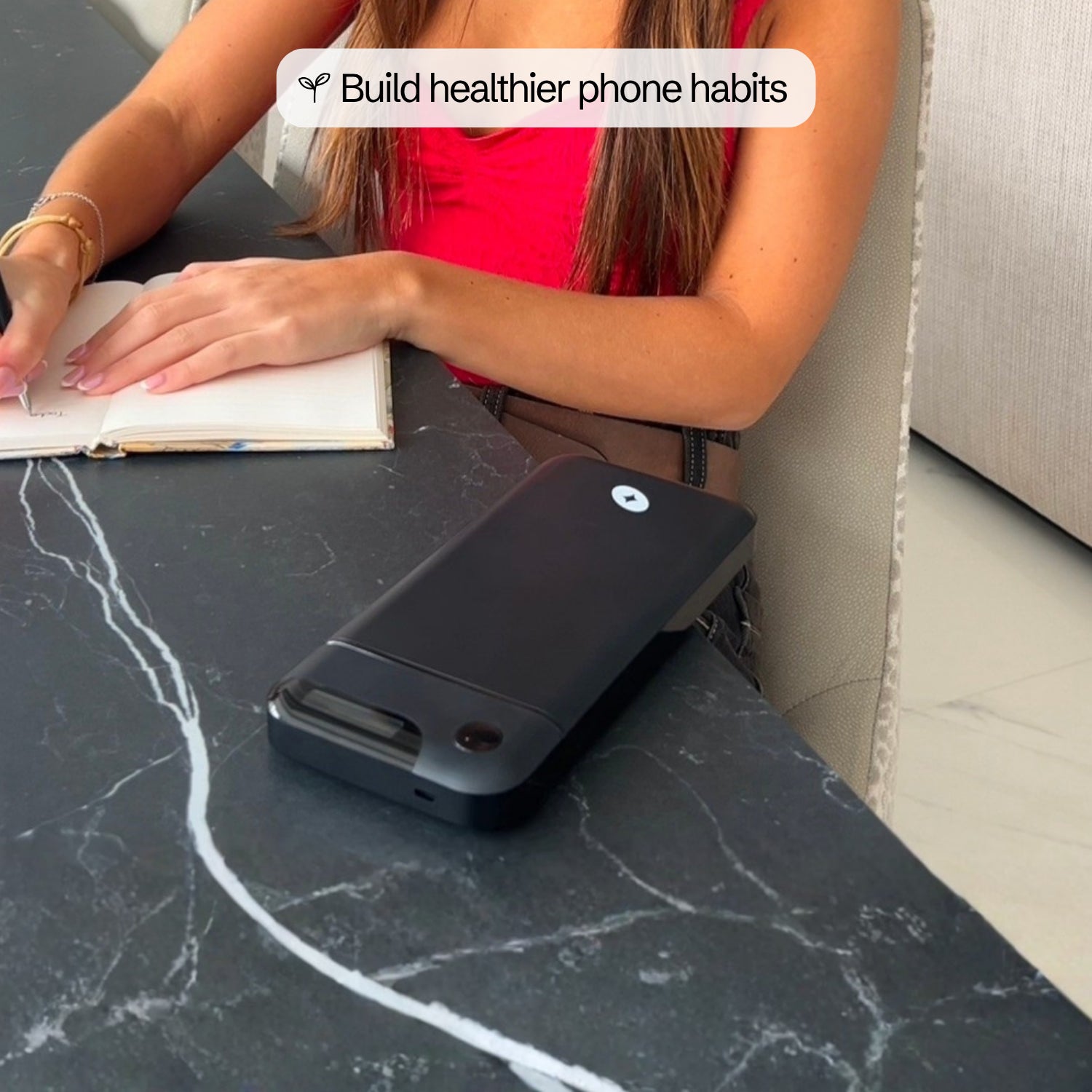 A woman journals at a table while her phone sits locked inside the Lockbox